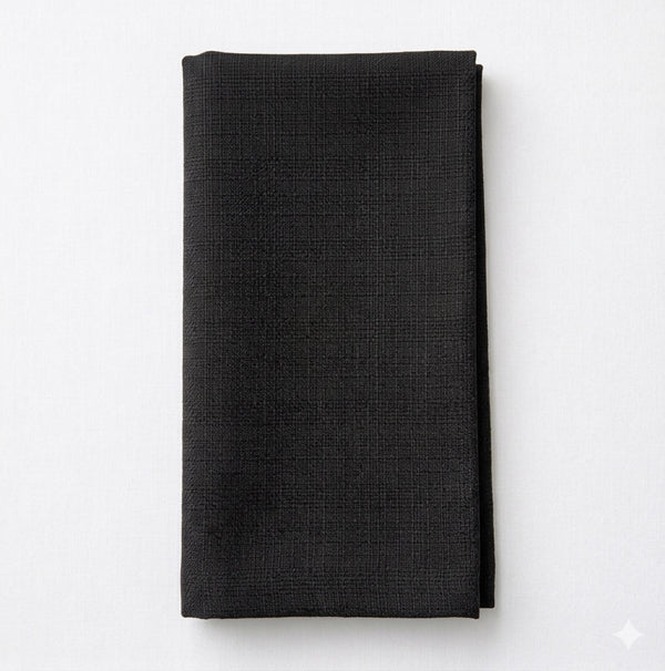 The Amelia Black Linen napkin, crafted with a textured pattern and elegant fabric, highlights quality craftsmanship as it rests neatly folded on a white surface.