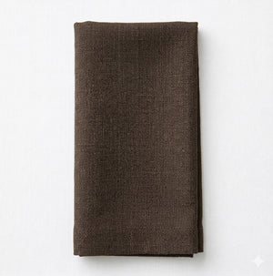 A neatly folded Amelia Brown Linen napkin rests on a light, solid surface.