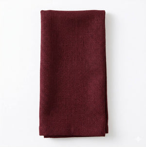 A neatly folded Amelia Burgundy Linen napkin, crafted from elegant fabric, rests on a white surface—ideal for an upscale event.