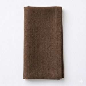 The Amelia Chocolate Linen is a neatly folded brown linen napkin with a textured finish, elegantly displayed on a plain white surface.