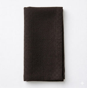 A neatly folded Amelia Dark Brown Linen napkin, made from elegant linen fabric, rests on a white surface.