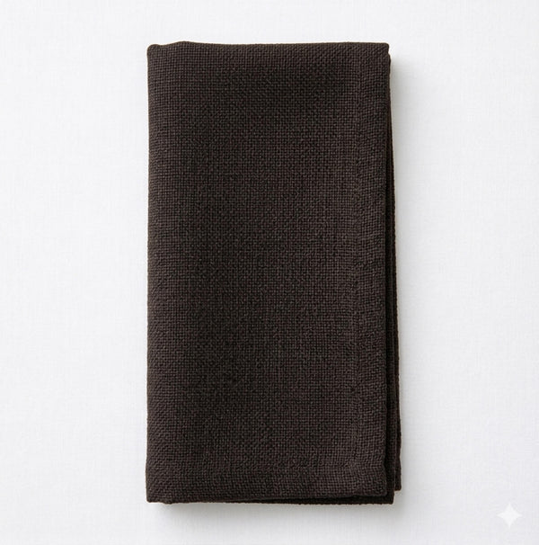 A neatly folded Amelia Dark Brown Linen napkin, made from elegant linen fabric, rests on a white surface.