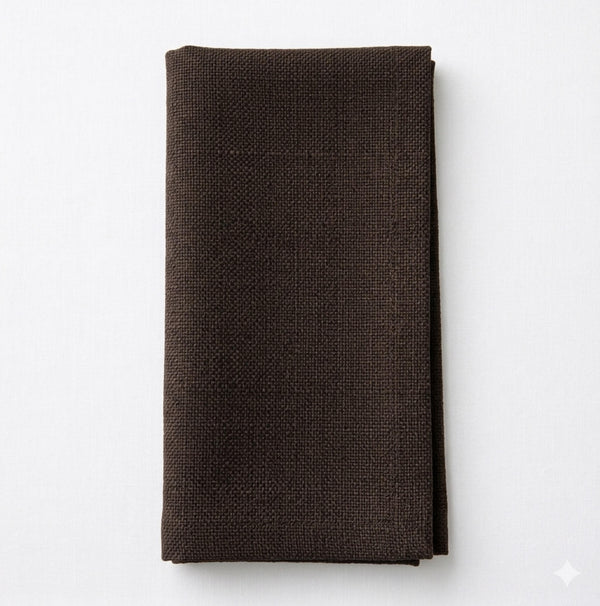 A neatly folded Amelia Dark Chocolate Linen napkin rests on a white surface, providing an elegant, textured fabric accent to any event setting.