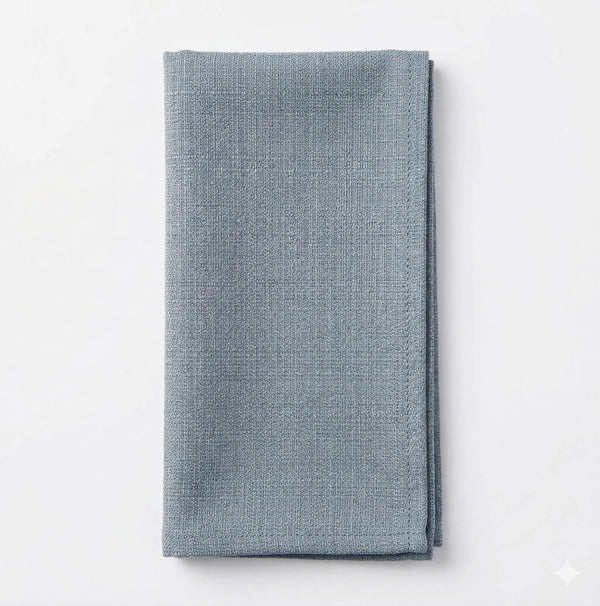 The Amelia Light Blue Linen napkin, elegantly textured and neatly folded, adds a refined fabric accent to any event decor. Displayed on a white background for sophisticated style.