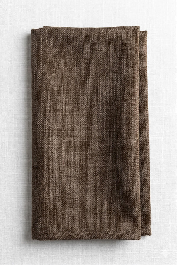 A neatly folded Amelia Light Brown Linen napkin, crafted from elegant fabric, rests on a white, subtly textured surface.