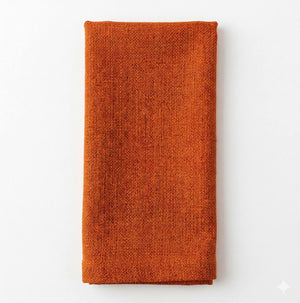 A neatly folded Amelia Orange Linen napkin rests on a plain white background, offering a textured and elegant fabric accent for any event setting.