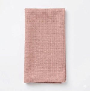 A neatly folded Amelia Pink Linen napkin rests on a plain white background, showcasing elegant textured fabric perfect for elevating any event setting.