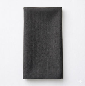 A neatly folded Amelia Slate Grey Linen napkin rests on a white surface, highlighting its elegant, textured fabric—ideal for adding sophistication to any refined event setting.