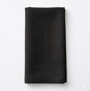 The Amelia Soft Black Linen napkin is neatly folded on a white surface, bringing an elegant fabric accent to any event setting.