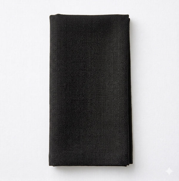 The Amelia Soft Black Linen napkin is neatly folded on a white surface, bringing an elegant fabric accent to any event setting.