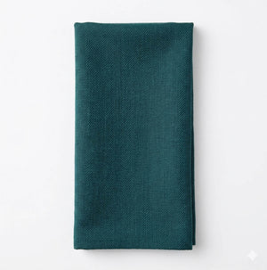 The Amelia Yucca Linen is a dark teal cloth napkin, neatly folded to showcase its elegant linen fabric and subtle herringbone pattern, displayed on a white background.