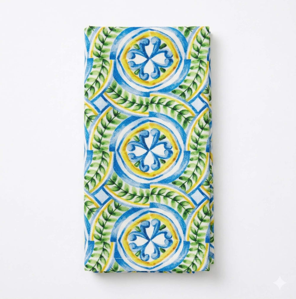 Amina Linen tablecloth features vivid blue, green, and yellow geometric and floral designs. Softly draping over the edges, it adds vibrant elegance to any table setting.