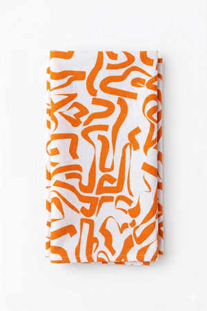 The Aria Linen exclusive collection features a folded white cloth with an abstract orange pattern of irregular, curving shapes, laid on a plain white background for a modern, elegant touch.