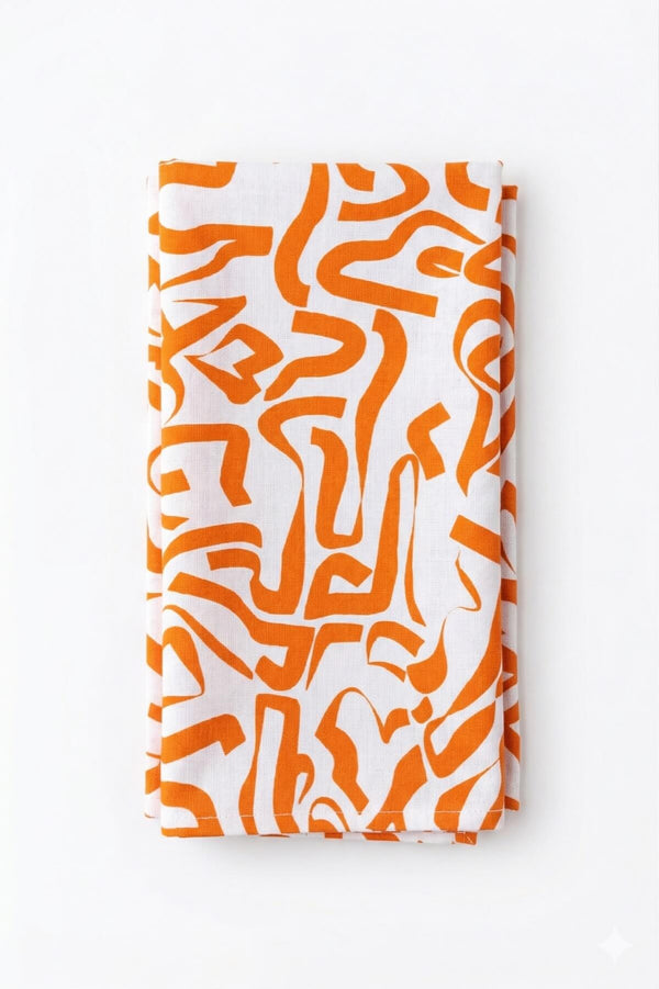 The Aria Linen exclusive collection features a folded white cloth with an abstract orange pattern of irregular, curving shapes, laid on a plain white background for a modern, elegant touch.