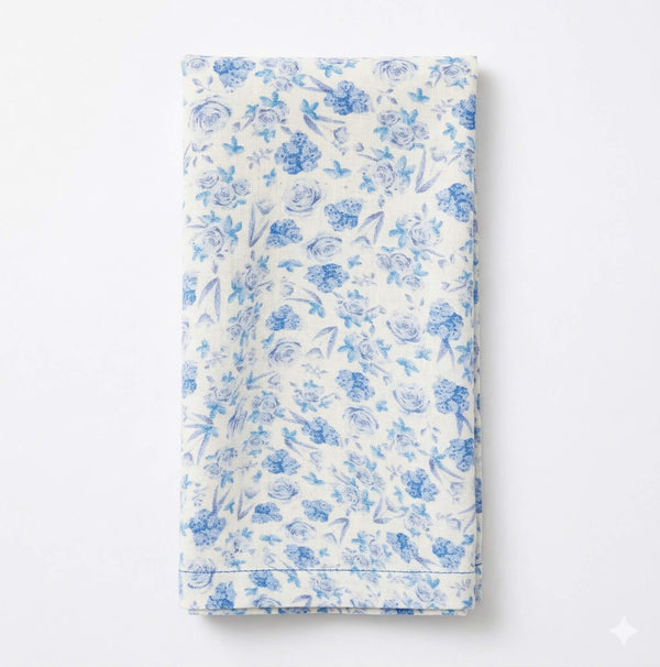 The Bella Linen white cloth napkin, featuring a delicate blue floral design, is neatly folded to enhance your table setting with elegance.
