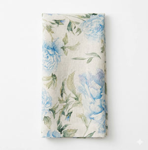 The Celeste Linen napkin features a watercolor-style floral pattern with blue flowers and green leaves on white, perfect for elegant table settings.
