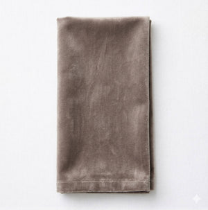 A neatly folded Charlotte Ash Grey Velvet napkin is placed on a light surface, showcasing its soft texture and subtle sheen.