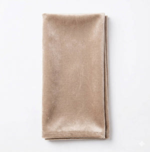 A neatly folded, rectangular Charlotte Beige Velvet napkin is placed on a white surface.