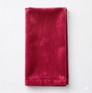 The Charlotte Burgundy Velvet napkin, neatly folded on a white surface, highlights its rich red color, soft texture, and smooth finish.