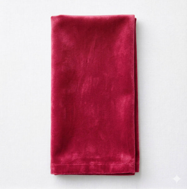 The Charlotte Burgundy Velvet napkin, neatly folded on a white surface, highlights its rich red color, soft texture, and smooth finish.