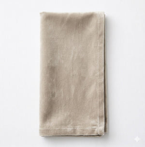 A neatly folded Charlotte Concrete Velvet cloth napkin with visible stitching along the edges, crafted from elegant fabric and placed on a white surface.