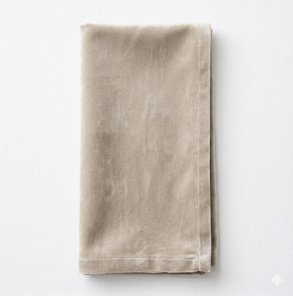 A neatly folded Charlotte Concrete Velvet cloth napkin with visible stitching along the edges, crafted from elegant fabric and placed on a white surface.