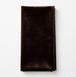 A Charlotte Dark Chocolate Velvet napkin is neatly folded and placed on a white surface.