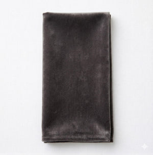 The Charlotte Dark Grey Velvet napkin, neatly folded on a light gray surface, adds an elegant touch to your table setting.