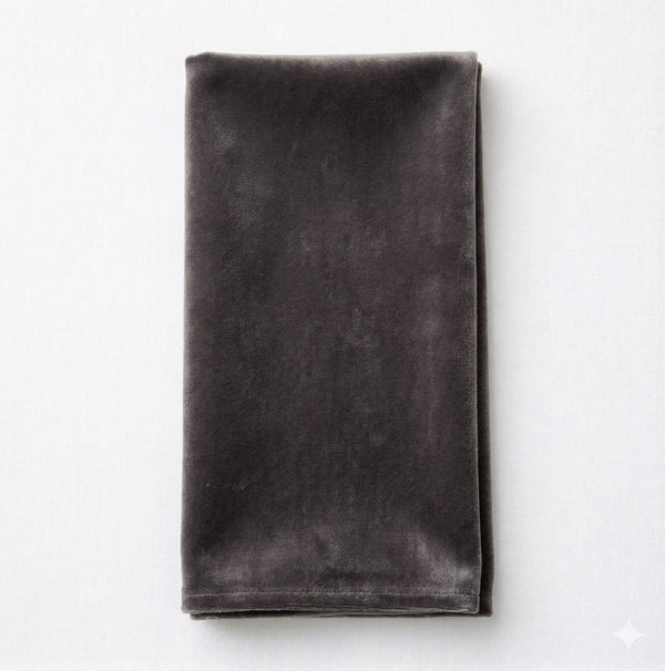 The Charlotte Dark Grey Velvet napkin, neatly folded on a light gray surface, adds an elegant touch to your table setting.