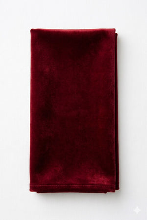 A Charlotte Dark Red Velvet napkin, neatly folded, lies on a white surface.