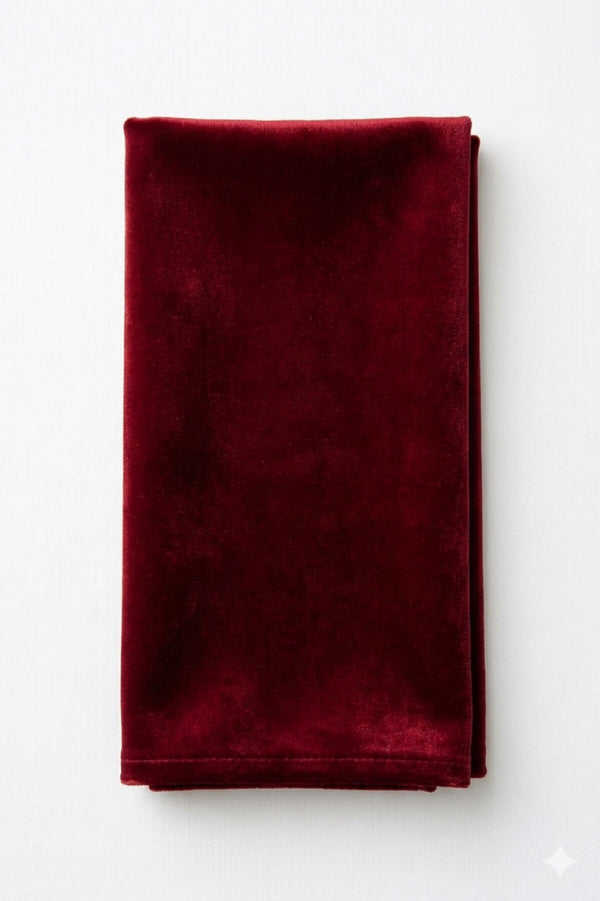 A Charlotte Dark Red Velvet napkin, neatly folded, lies on a white surface.