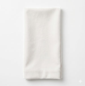 A neatly folded Charlotte Light Beige Velvet napkin, crafted from elegant fabric, is placed on a plain white background.