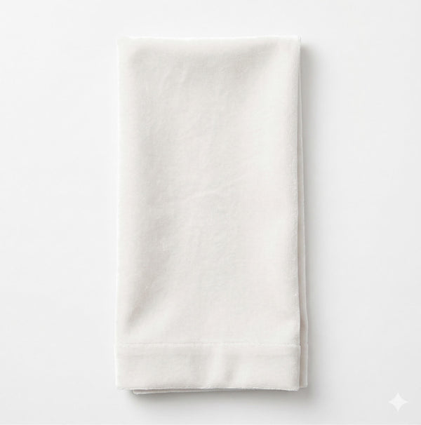 A neatly folded Charlotte Light Beige Velvet napkin, crafted from elegant fabric, is placed on a plain white background.