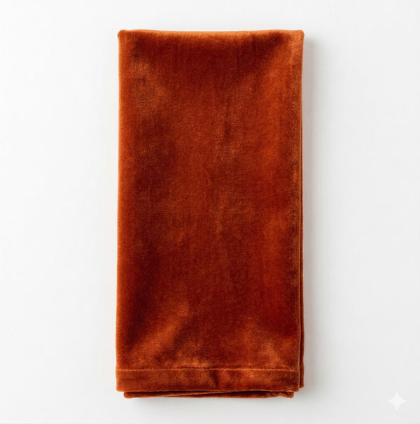 A folded napkin in a rich, deep rust hue highlights the luxurious Charlotte Orange Velvet fabric.