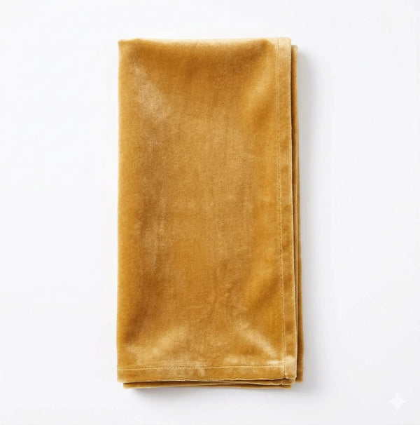 A neatly folded, gold velvet napkin made from Charlotte Sand Velvet lies on a white surface, highlighting its elegant fabric.