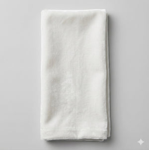 A neatly folded Charlotte White Velvet towel rests on a light gray surface, showcasing its soft, smooth texture, clean edges, and elegant sheen as proof of fine craftsmanship.
