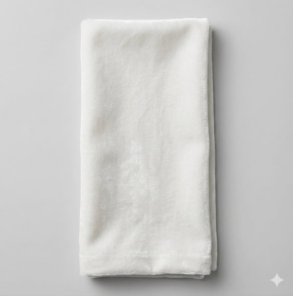 A neatly folded Charlotte White Velvet towel rests on a light gray surface, showcasing its soft, smooth texture, clean edges, and elegant sheen as proof of fine craftsmanship.