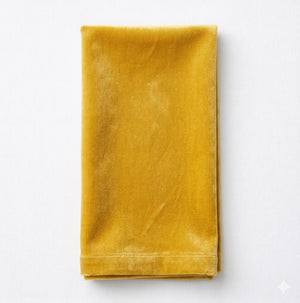 A neatly folded Charlotte Yellow Velvet napkin rests on a white surface, highlighting its soft velvet texture—ideal for adding luxury to any elegant event or table setting.