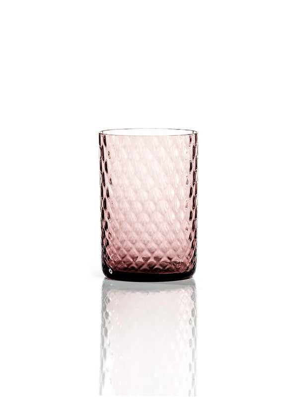 The Alba Plum Tumbler, featuring a diamond-textured, transparent pink design, stands upright on a reflective white background and exemplifies modern luxury glassware.