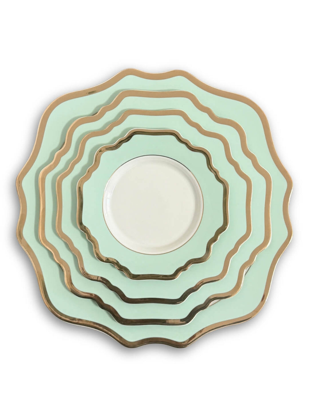 The Colette Green Plate Range includes five scalloped-edge plates in graduating sizes, stacked together. Featuring a light green hue, gold trim, and a white center, they add modern elegance to any setting. The background is plain white.