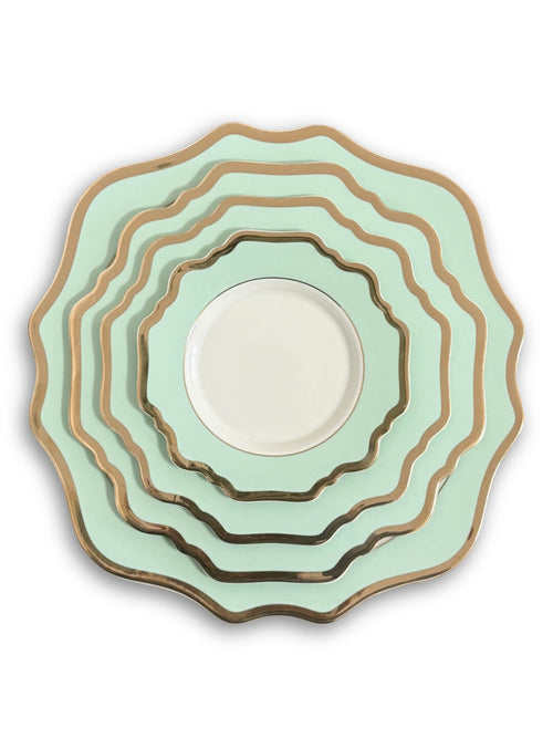 The Colette Green Plate Range includes five scalloped-edge plates in graduating sizes, stacked together. Featuring a light green hue, gold trim, and a white center, they add modern elegance to any setting. The background is plain white.