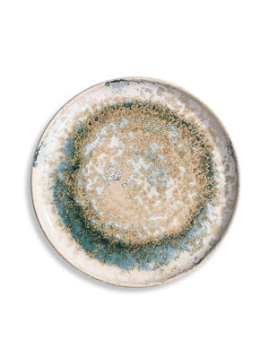 The Cove Plate Range features a round ceramic plate with a mottled, textured design in beige, blue, and green tones. This artisanal dinnerware piece has a thin, slightly raised edge and is shown from above on a white background.