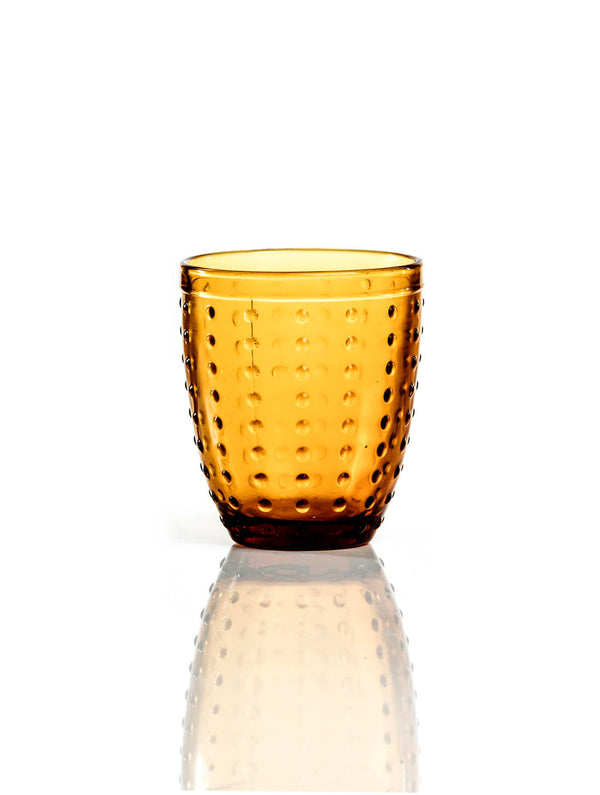 The Dotty Amber Tumbler, with its dotted textured glass that catches the light, sits elegantly on a reflective white surface—perfect for autumn gatherings.