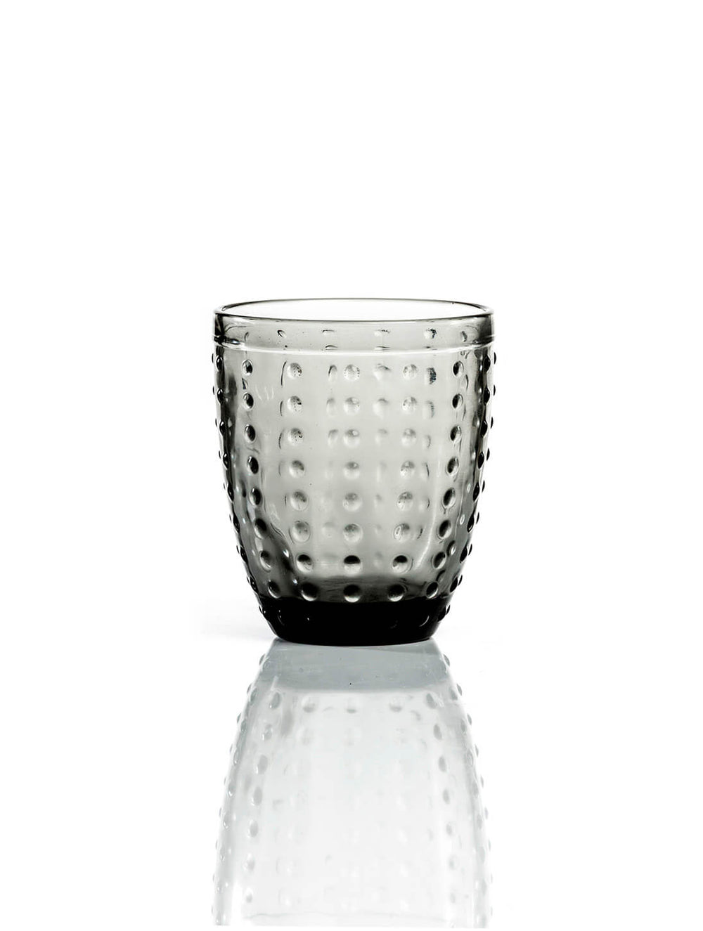 The Dotty Smoke Tumbler features modern grey-tinted glass with a rounded shape and textured dimpled surface, shown on a white background with a subtle reflection.