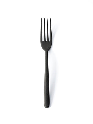 A Jett Cutlery Range matte black fork with four tines stands upright on a plain white background, highlighting its sleek, modern design.