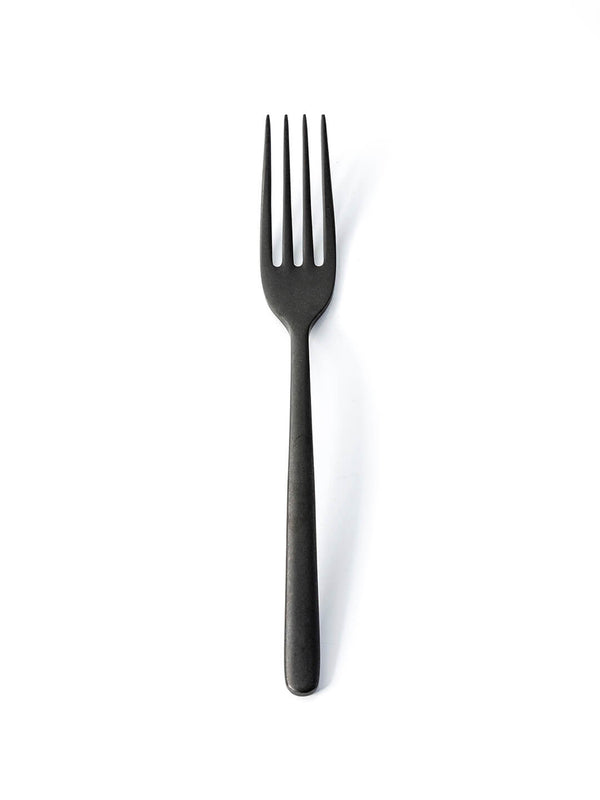 A Jett Cutlery Range matte black fork with four tines stands upright on a plain white background, highlighting its sleek, modern design.