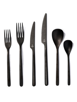 Six matte black pieces from the Jett Cutlery Range‚Äîtwo forks, two knives, a large spoon, and a small spoon‚Äîare arranged in a row on a white background, showcasing this elegant modern set for any table.