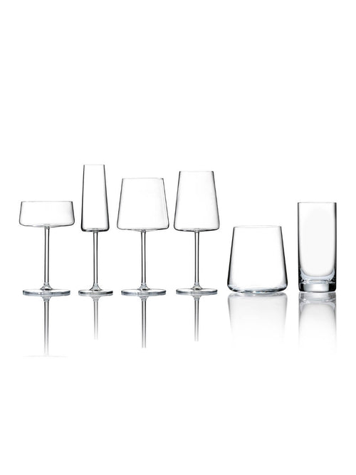A row of six clear, empty glasses from the Lola Glassware Range—featuring wine, cocktail, and tumbler styles—is elegantly arranged on a reflective white surface.