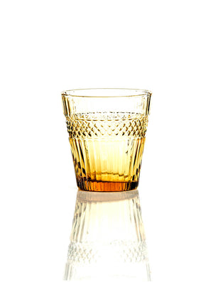 The Margot Amber Tumbler, featuring textured diamond-like patterns around the upper half, sits on a reflective white surface—perfect for autumn gatherings.