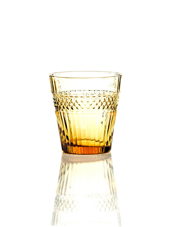 The Margot Amber Tumbler, featuring textured diamond-like patterns around the upper half, sits on a reflective white surface—perfect for autumn gatherings.